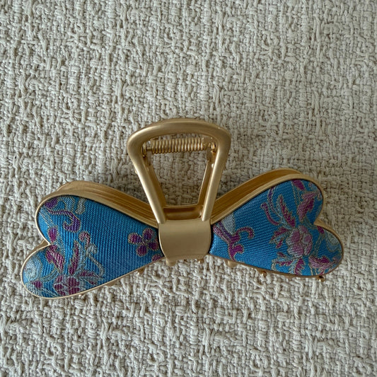 Blue Floral Bow Hair Claw Clip by JOFAE Kyoto. Scalloped bow silhouette; Blue textile with purple floral motifs; Smooth gold-tone centre; Claw fastening.