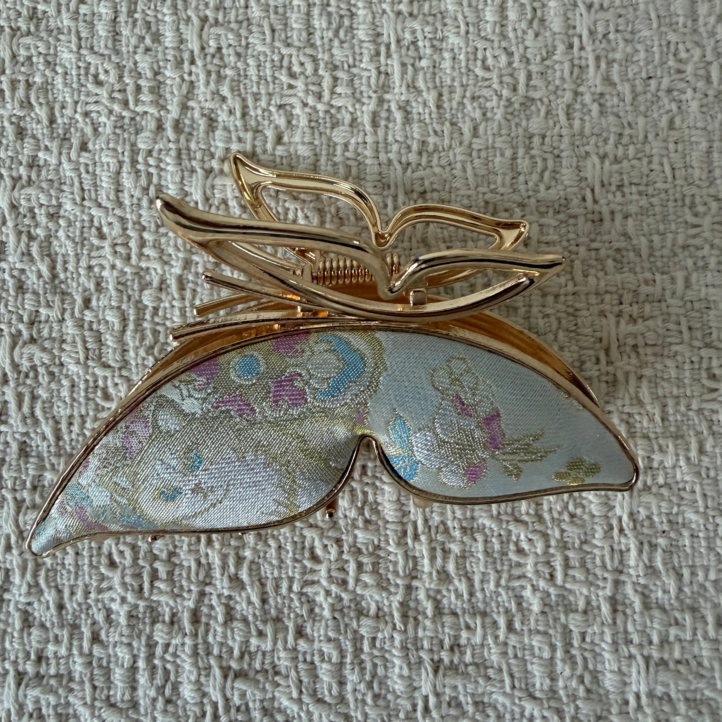 Ivory Butterfly Hair Claw Clip by JOFAE Kyoto. Sculptural butterfly silhouette; Ivory textile with pastel motifs; Open gold-tone upper wings; Claw fastening.