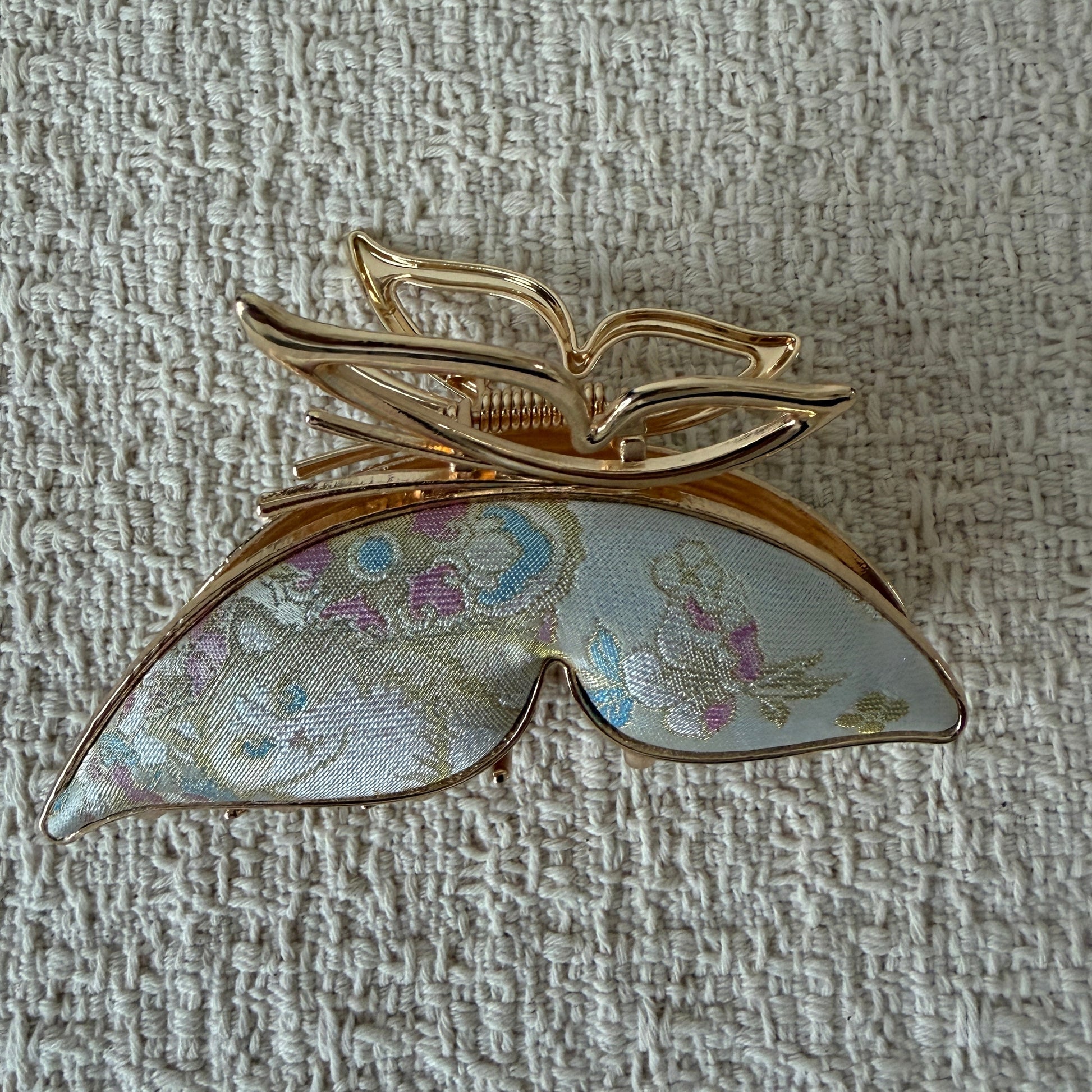 Ivory Butterfly Hair Claw Clip by JOFAE Kyoto. Sculptural butterfly silhouette; Ivory textile with pastel motifs; Open gold-tone upper wings; Claw fastening.