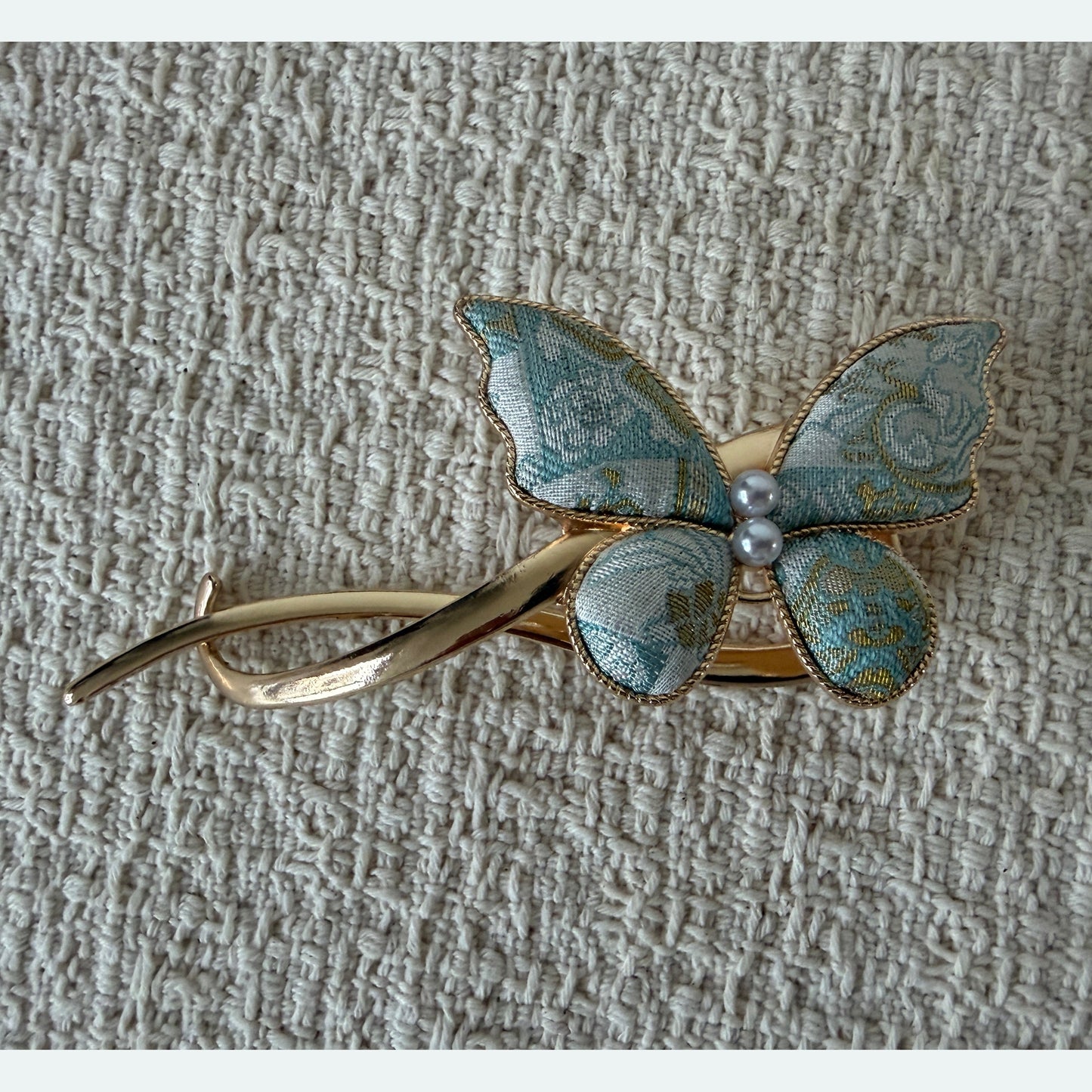 Pale Blue Butterfly Hair Claw Clip by JOFAE Kyoto. Asymmetrical butterfly design; Pale blue patterned textile wings; Two pearl-effect centre beads; Sweeping open gold-tone frame.