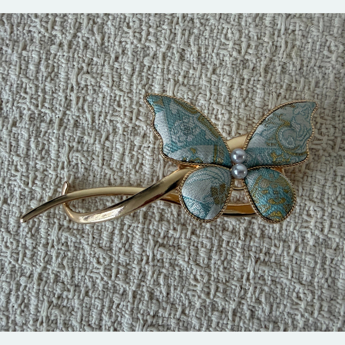 Pale Blue Butterfly Hair Claw Clip by JOFAE Kyoto. Asymmetrical butterfly design; Pale blue patterned textile wings; Two pearl-effect centre beads; Sweeping open gold-tone frame.