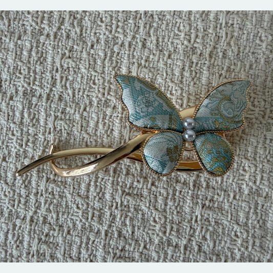 Pale Blue Butterfly Hair Claw Clip by JOFAE Kyoto. Asymmetrical butterfly design; Pale blue patterned textile wings; Two pearl-effect centre beads; Sweeping open gold-tone frame.