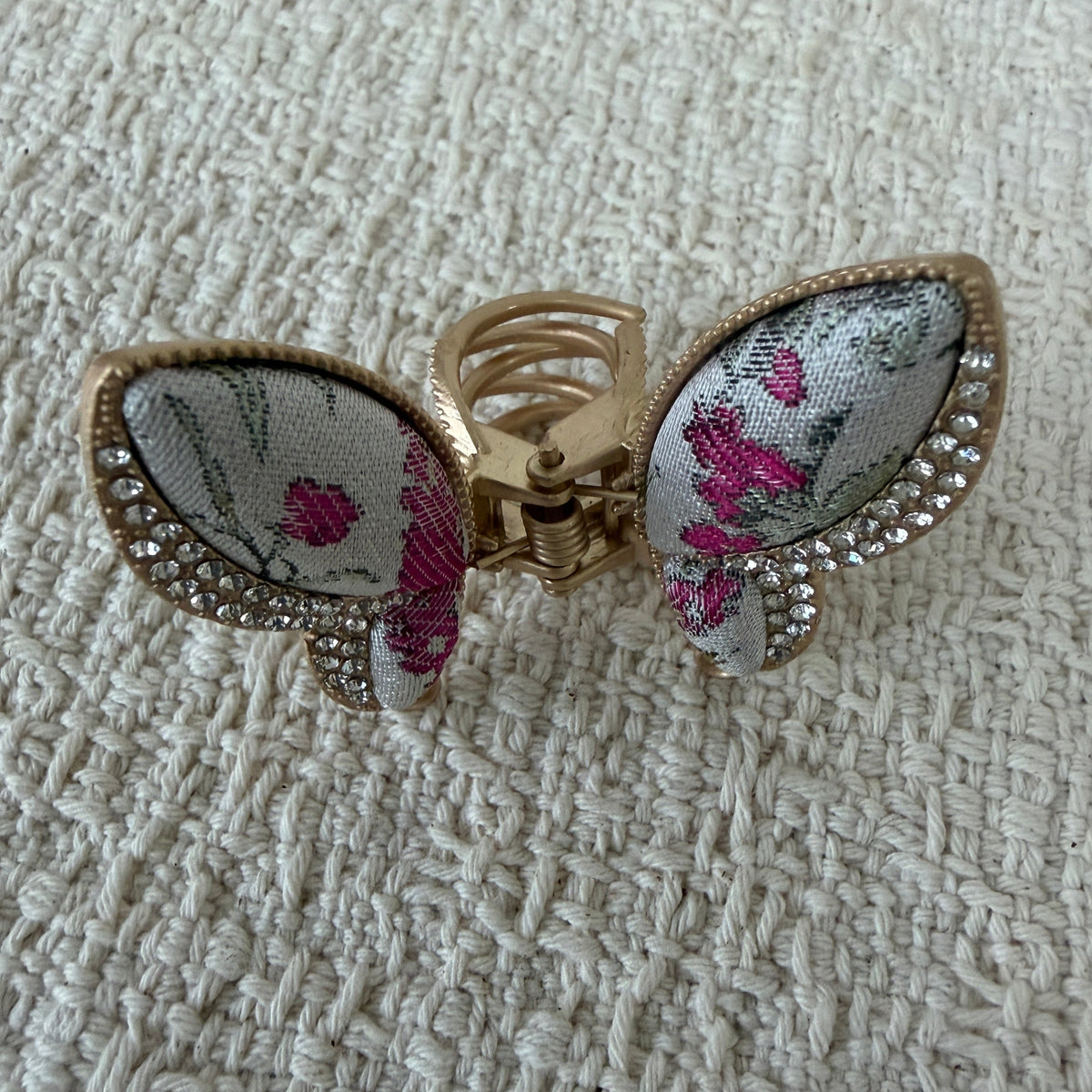 Ivory Floral Butterfly Hair Claw Clip by JOFAE Kyoto. Butterfly silhouette; Ivory textile with pink floral motifs; Clear sparkling wing accents; Gold-tone claw frame.