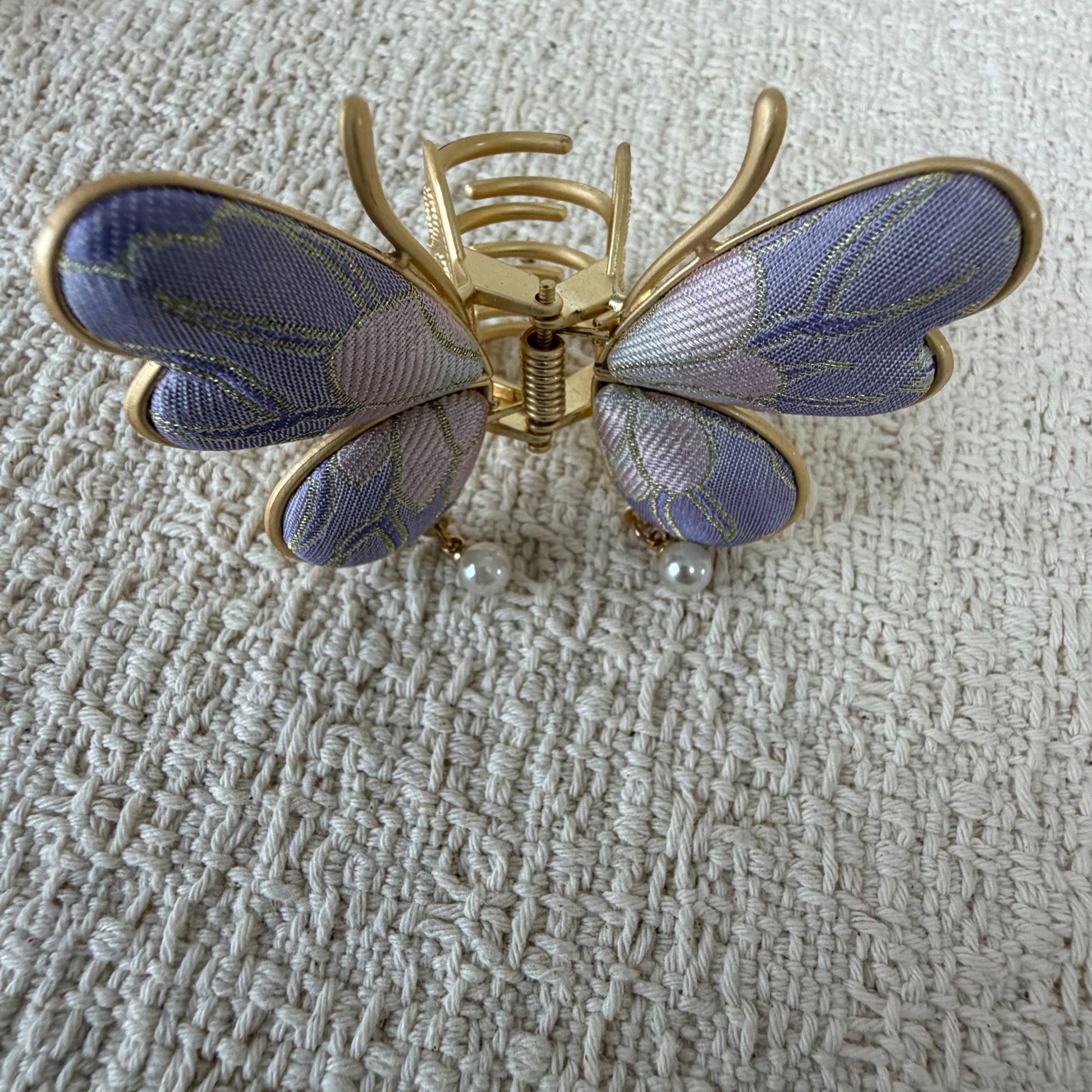Lavender Butterfly Hair Claw Clip with Pearl-Effect Drops by JOFAE Kyoto. Four-wing butterfly silhouette; Lavender patterned textile; Two pearl-effect drops; Gold-tone antennae and claw frame.