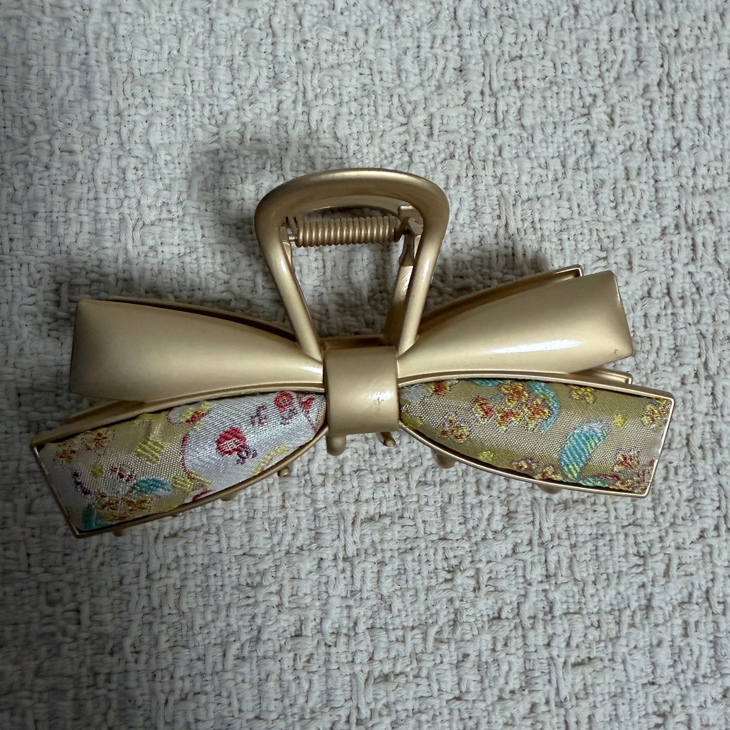 Ivory Layered Bow Hair Claw Clip by JOFAE Kyoto. Layered bow silhouette; Ivory textile with multicoloured motifs; Sculpted gold-tone loops; Claw fastening.